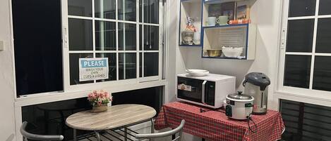 Una pequeña cocina americana equipada con microondas, hervidor de agua y ventilador. Hay un cartel solicitando a los huéspedes que laven sus propios vasos y platos.