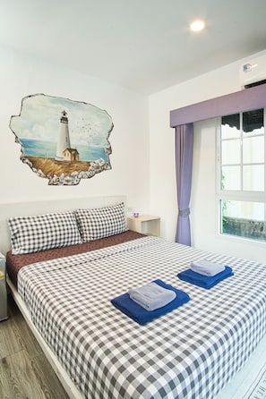 A hotel room with a checkered bedspread, a pillow, a nightstand, a lamp, a window with curtains, and a wall decoration of a lighthouse. - comfy crib hostel  (Bangkok)