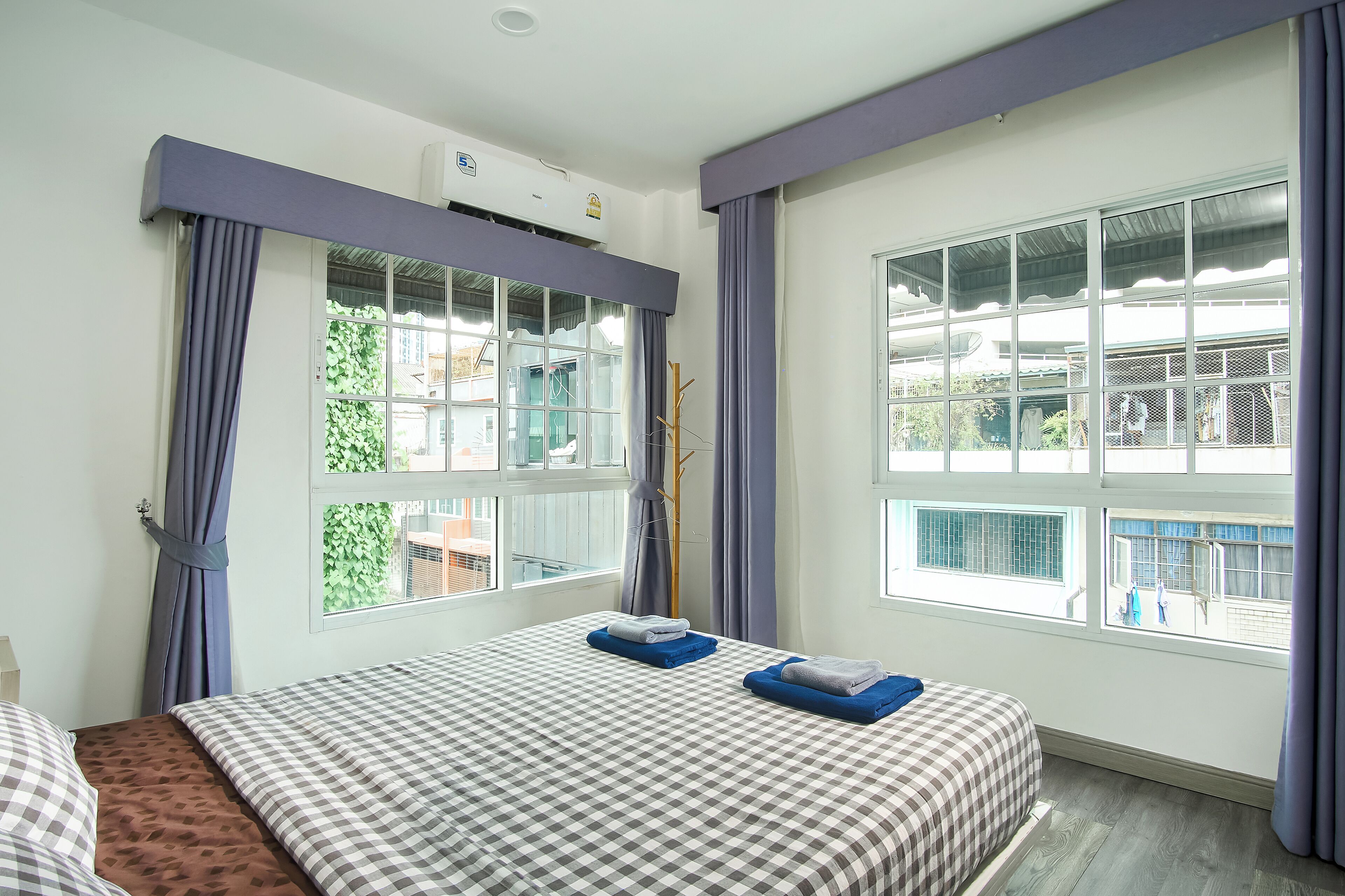 A hotel room with a checkered bedspread, a window with curtains, and a view of the outside.