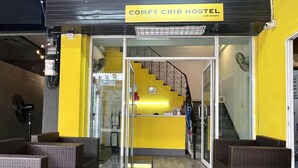 A hostel interior with wicker furniture, a reception desk, and a staircase leading to upper floors. - comfy crib hostel  (Bangkok)