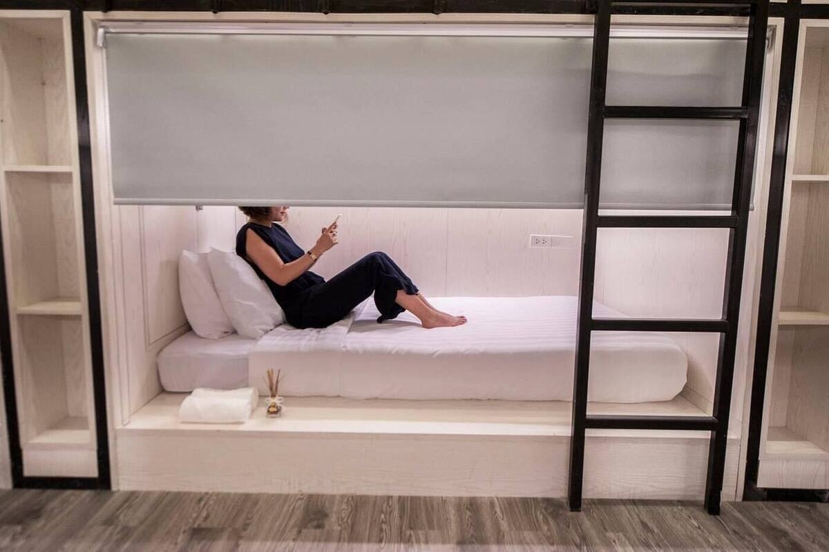 A woman sitting on a white sofa in a room with a wooden floor, a black ladder, and a white wall.