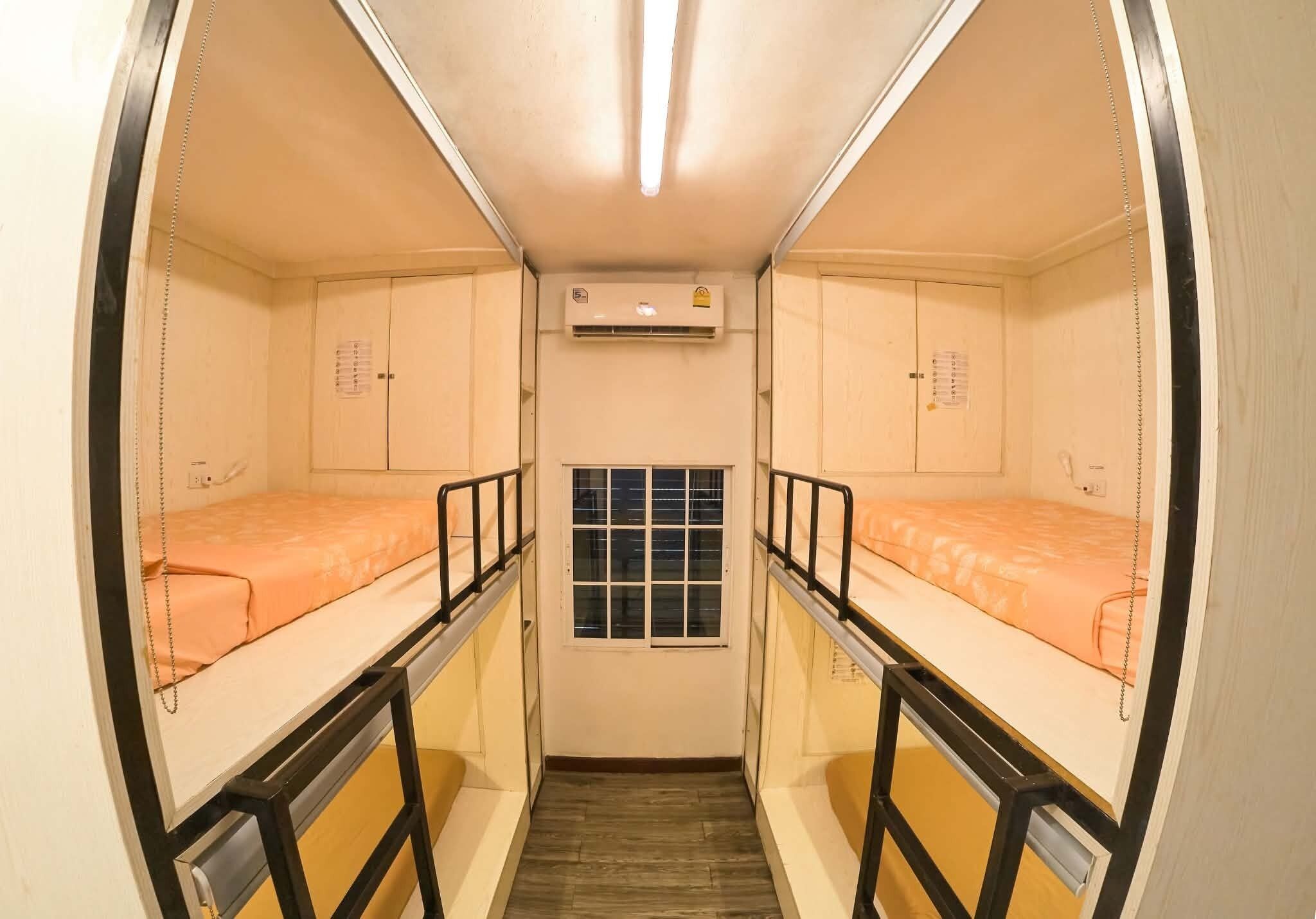 A narrow room with two beds, a window, and an air conditioning unit.