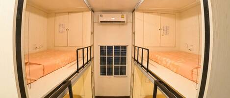 A narrow room with two beds, a window, and an air conditioning unit.