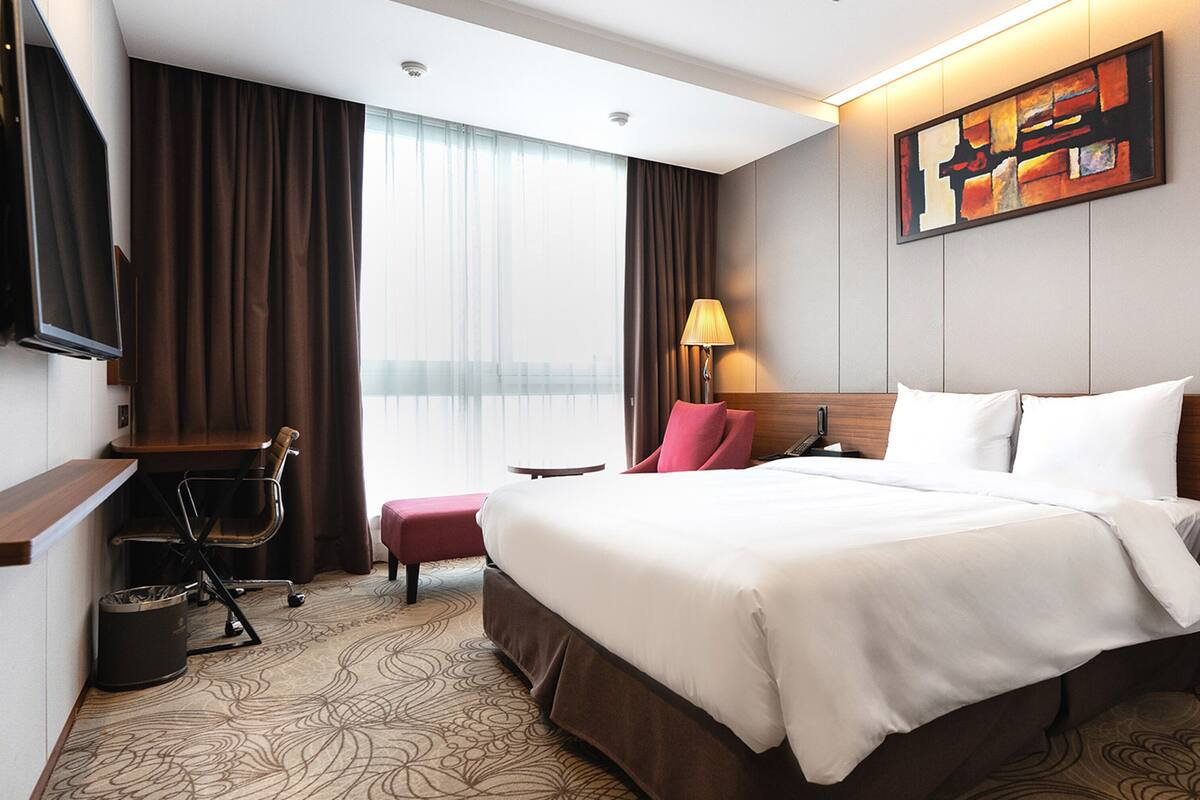 Une chambre d’hôtel avec un grand lit, un bureau, une chaise, une lampe et un tableau au mur.