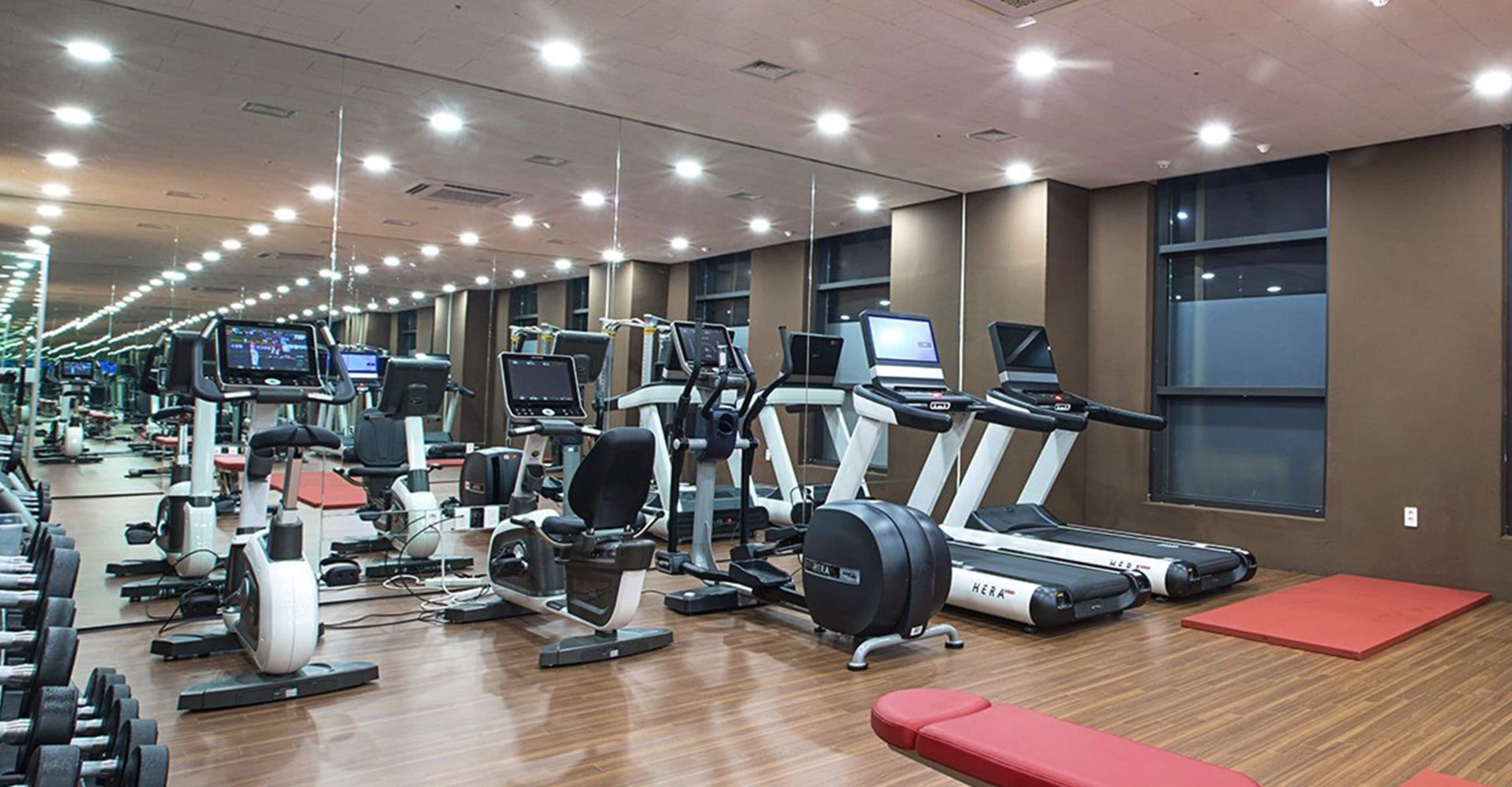A gym with various exercise machines, mirrors, and a wooden floor.