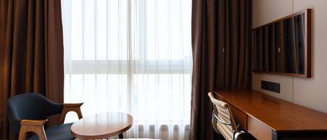 A hotel room with a bed, a desk, a chair, a round table, and a TV.