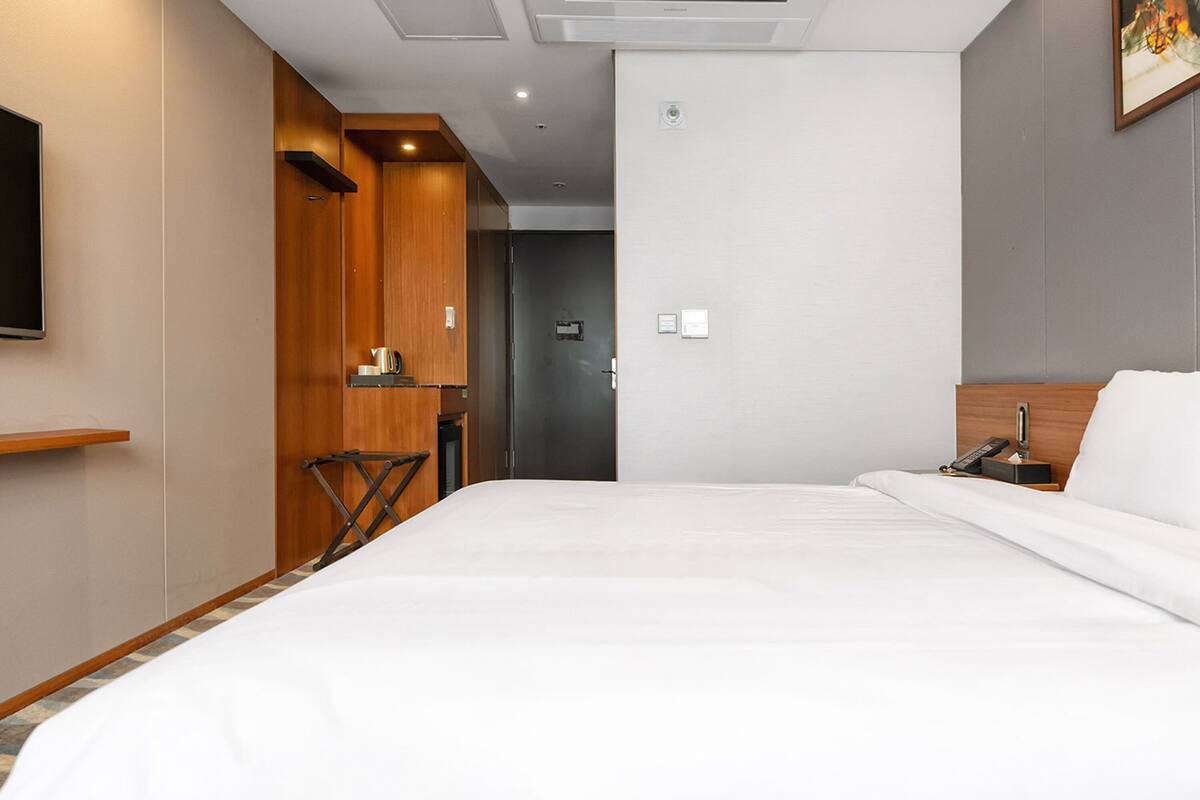 Une chambre d’hôtel dotée d’un grand lit, d’un téléviseur à écran plat fixé au mur, d’une armoire en bois et d’un petit coin cuisine.