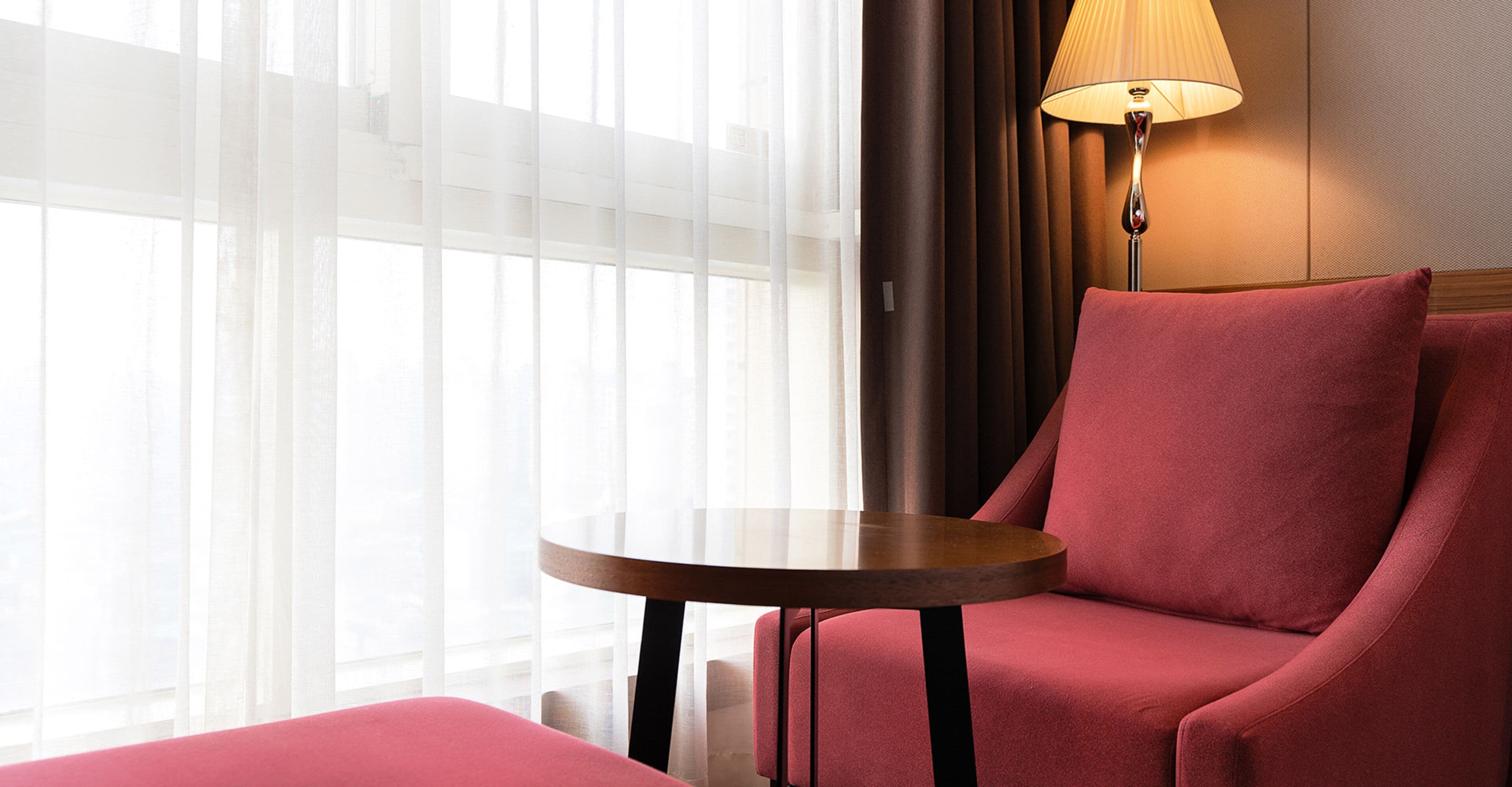Una habitación con una mesa redonda, una silla roja, una lámpara y cortinas traslúcidas.