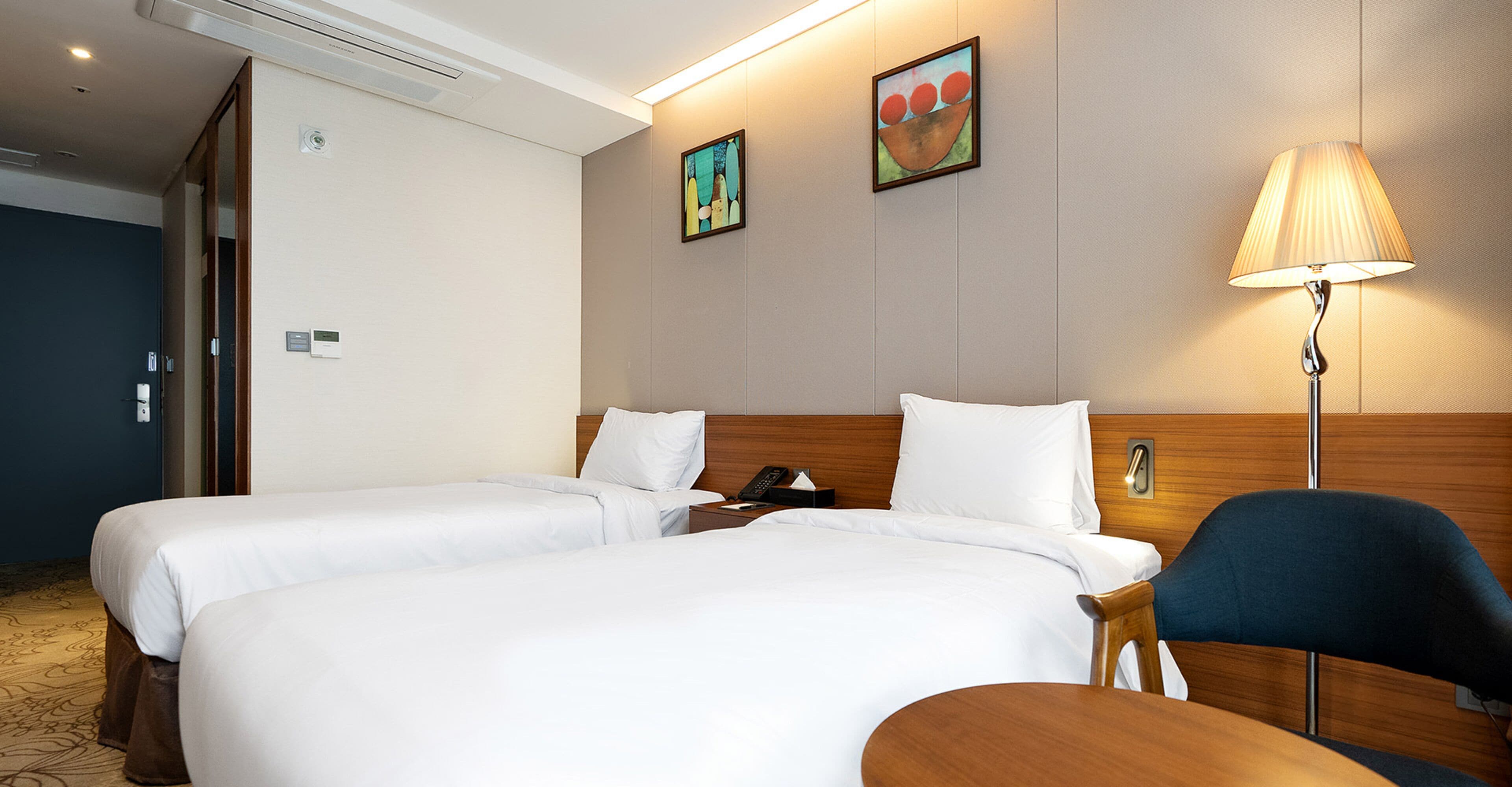 Una habitación de hotel con dos camas, una mesita de noche con lámpara y una silla.