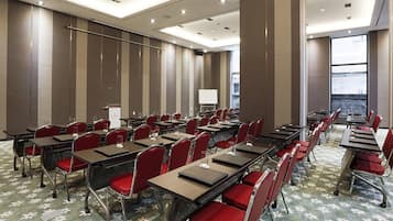 Un salón de conferencias con filas de mesas y sillas, un atril y un amplio ventanal con vistas.