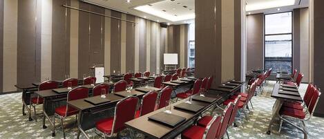 A conference room with rows of tables and chairs, a podium, and a large window offering a view.