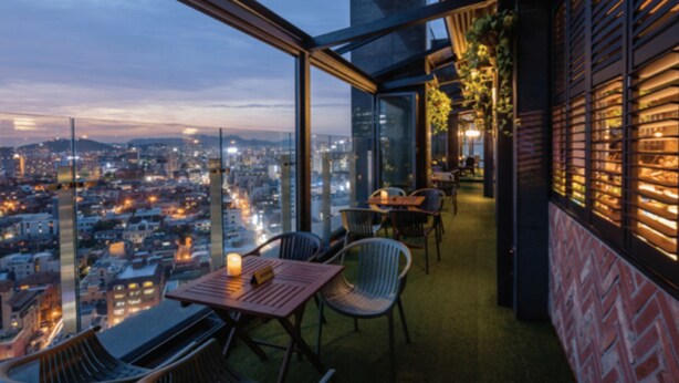 A modern rooftop bar with a panoramic city view, furnished with chairs and tables, and a glass railing overlooking the cityscape. - Gloucesterhotel Jeonju  (Jeonju)