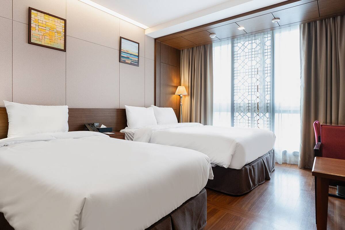 Une chambre d’hôtel avec deux lits, un bureau, une chaise, une lampe et une vue sur l’extérieur.