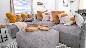Una sala moderna con un sofá seccional gris, bandejas de madera y un tapete a rayas.