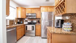 Una cocina con armarios de madera, electrodomésticos de acero inoxidable, encimeras de granito y un espacio para vinos empotrado.