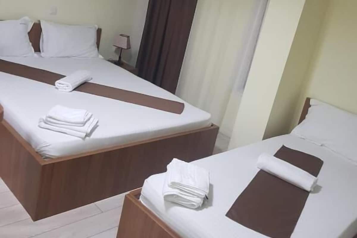 Habitación de hotel con dos camas, cada una con estructura de madera y ropa blanca. Hay un cuadro en la pared y una ventana con cortinas.