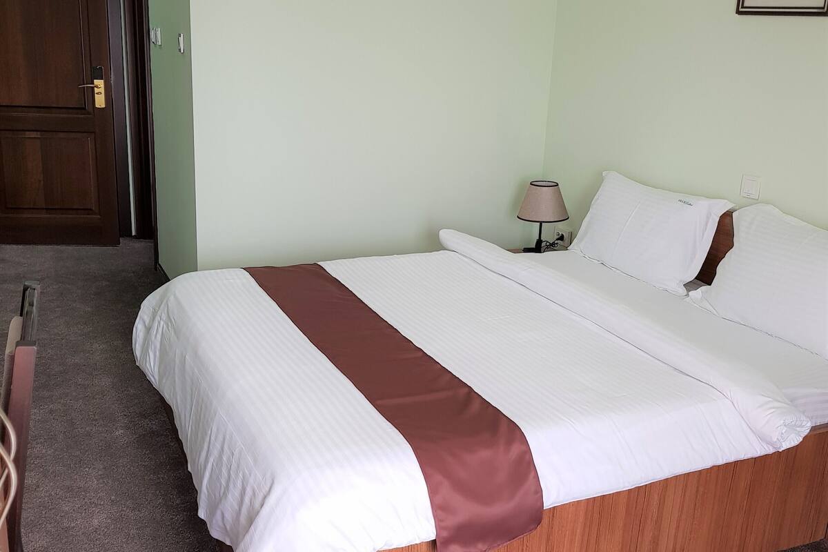 Una cama bien tendida con un detalle en tono marrón, un cabecero de madera y una mesita de noche con una lámpara.