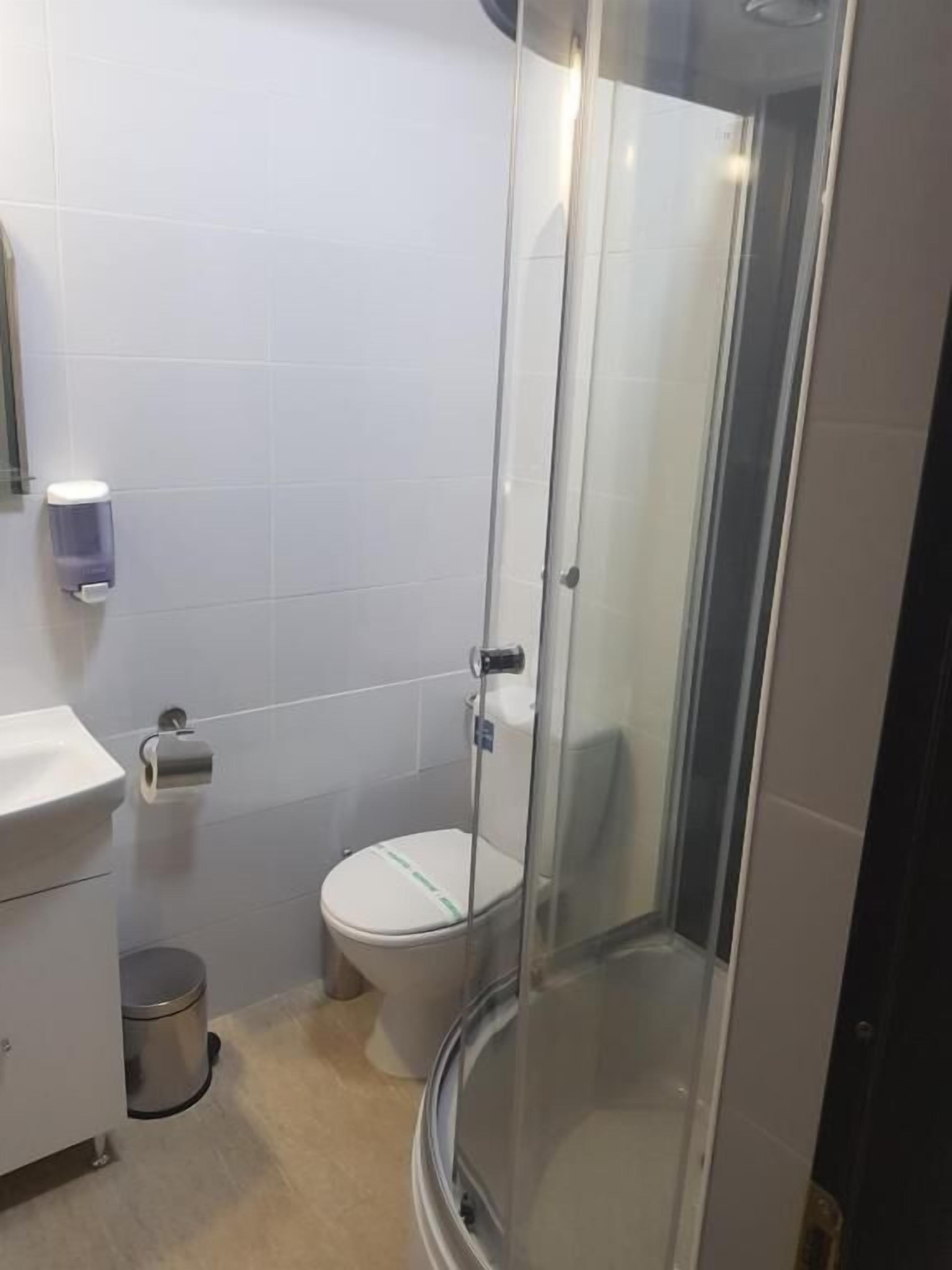 Un bagno moderno con doccia a vetro, un water e un lavandino con cestino.