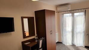 A hotel room with a desk, chair, wardrobe, television, and a window with sheer curtains. - Villa Lotus (Deva)
