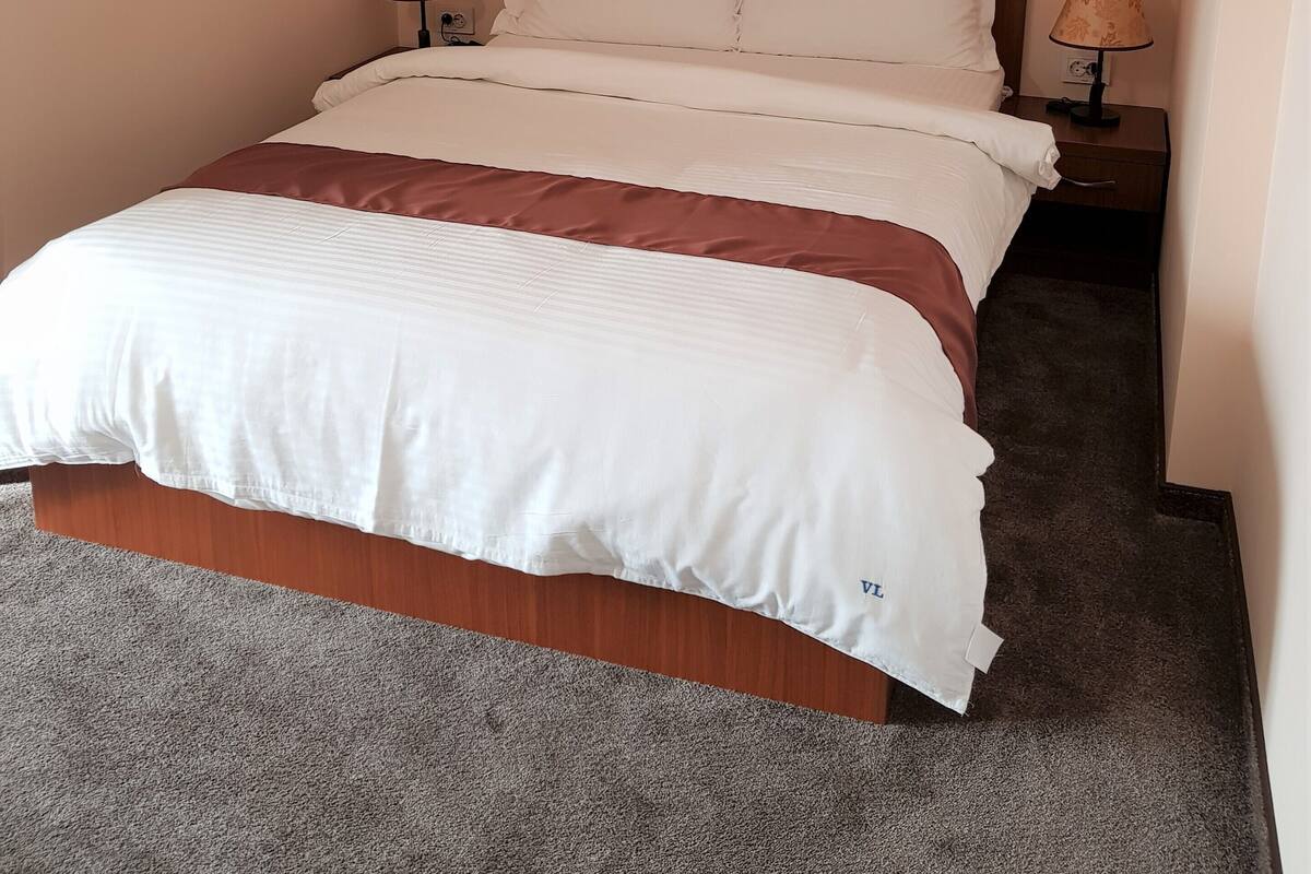 Una cama bien hecha con ropa de cama blanca y marrón, dos lámparas de noche y una obra de arte floral enmarcada en la pared.