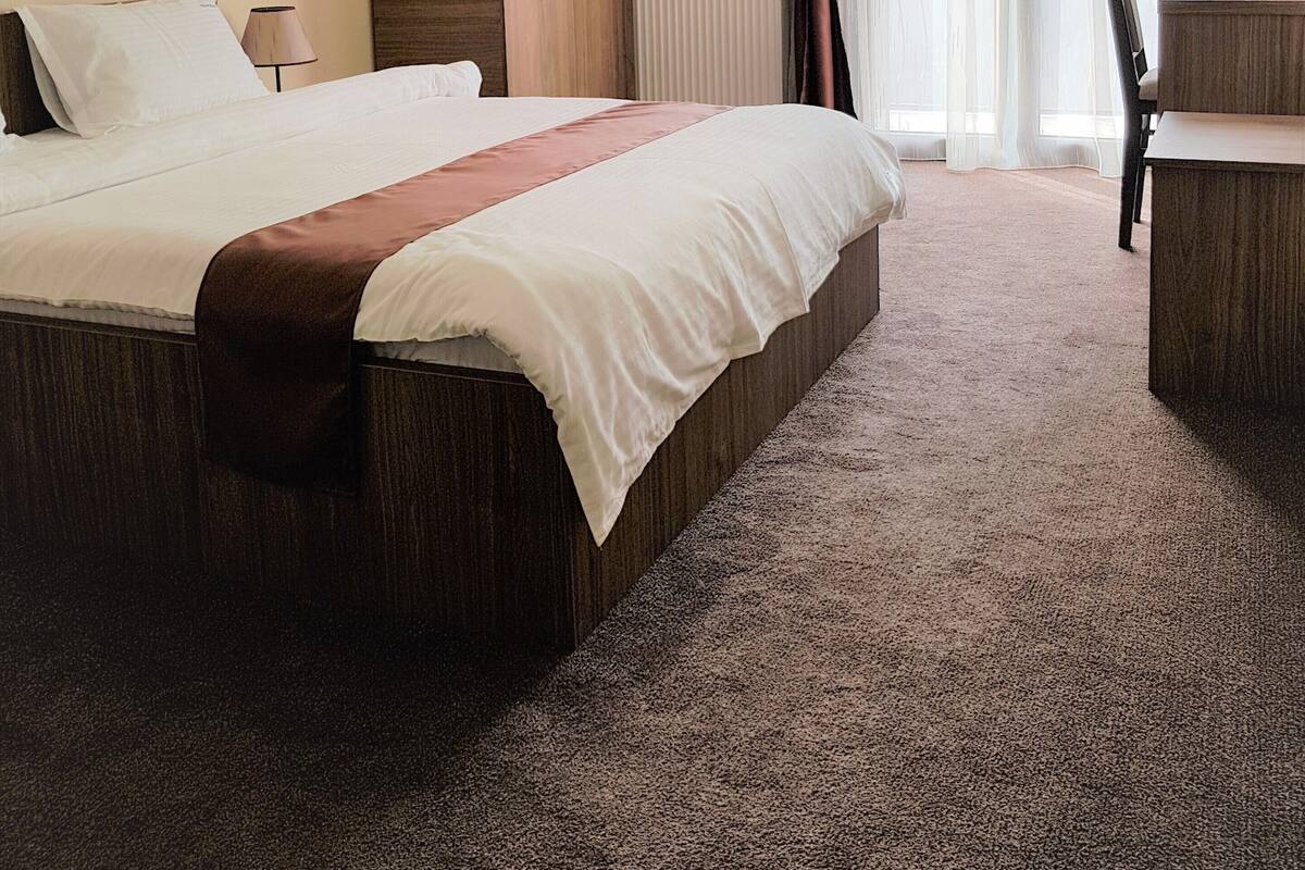 Una habitación de hotel con una cama grande, un armario de madera, un escritorio y una ventana con cortinas.