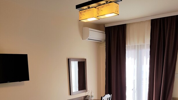 A hotel room with two beds, a desk, a chair, a flat-screen TV, a mirror, and a window with curtains. - Villa Lotus (Deva)