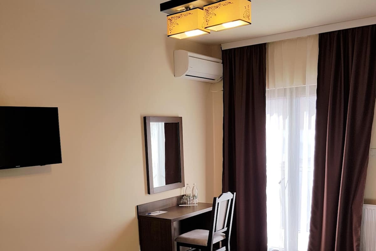 Habitación de hotel con dos camas, un escritorio, una silla, un televisor de pantalla plana, un espejo y una ventana con cortinas.
