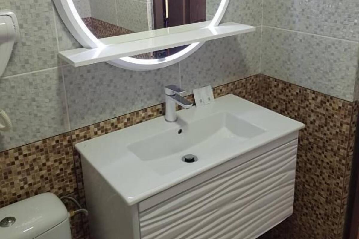 Un baño con un lavabo blanco, un espejo con luz y baldosas estampadas.