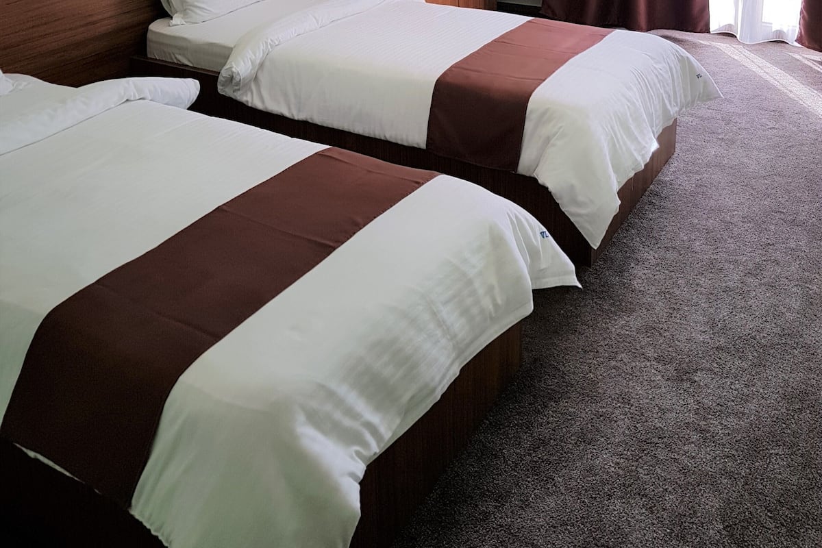 Una habitación de hotel con dos camas, un armario de madera, una lámpara y un ventanal grande con cortinas.