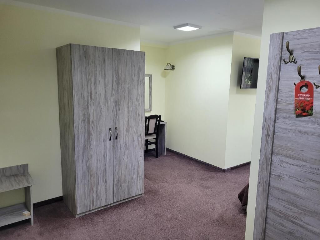 A room with a wardrobe, a chair, a small table, and a wall-mounted TV.