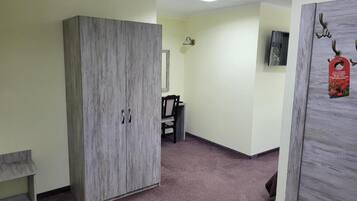 A room with a wardrobe, a chair, a small table, and a wall-mounted TV.
