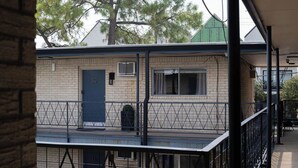 Un edificio de dos plantas con fachada de ladrillo, una puerta azul y un balcón con barandilla de metal.