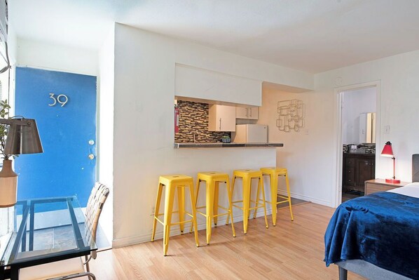 Un apartamento moderno con cocina, cuatro taburetes amarillos, una cama con cubrecolcha azul y una puerta azul con el número 39.