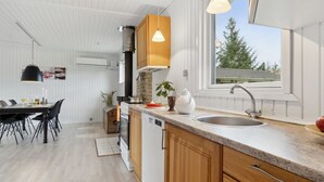A modern kitchen with wooden cabinets, a granite countertop, a built-in stove, and a window with a view of trees.