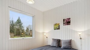 A bedroom with a large window, two wall-mounted lamps, and a bed with a grey quilt.