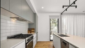 Een moderne keuken met witte kastjes, een gasfornuis, een vaatwasser en een houten vloer.