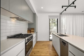 A modern kitchen with white cabinetry, a gas stove, a dishwasher, and a wooden floor. - 'Coastal Elegance, Torquay' (Torquay)