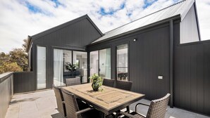Ein modernes Haus mit Terrasse, einem Esstisch und Korbstühlen.