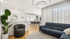 Een moderne woonkamer met een grijze bank, een ronde tafel en een grote plant.