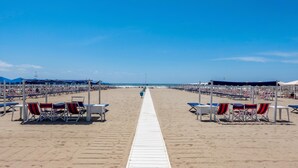 A beach with a white walkway leading to the sea, rows of beach chairs, and umbrellas.