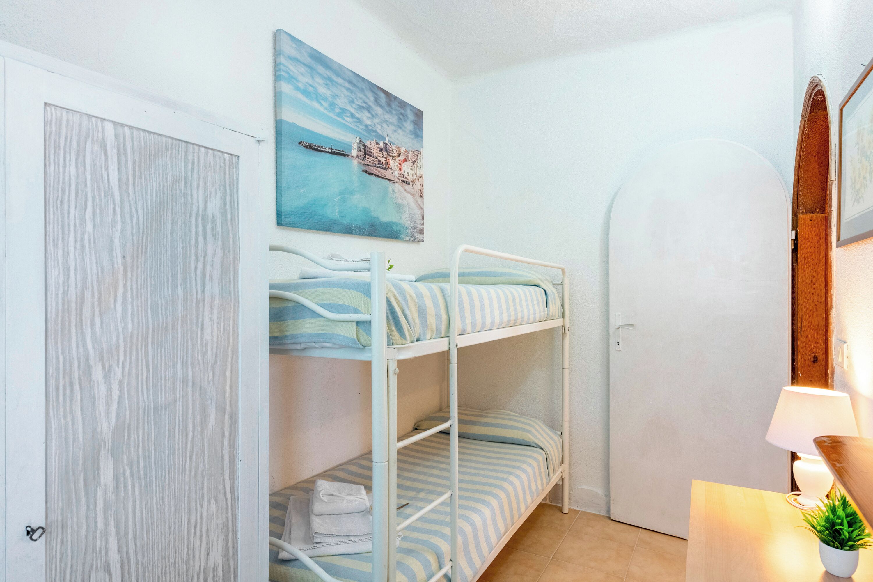 A bunk bed room with a coastal painting, a wooden door, and a bedside lamp.