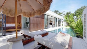 A modern outdoor pool area with lounge chairs, a wooden table, and a straw umbrella.