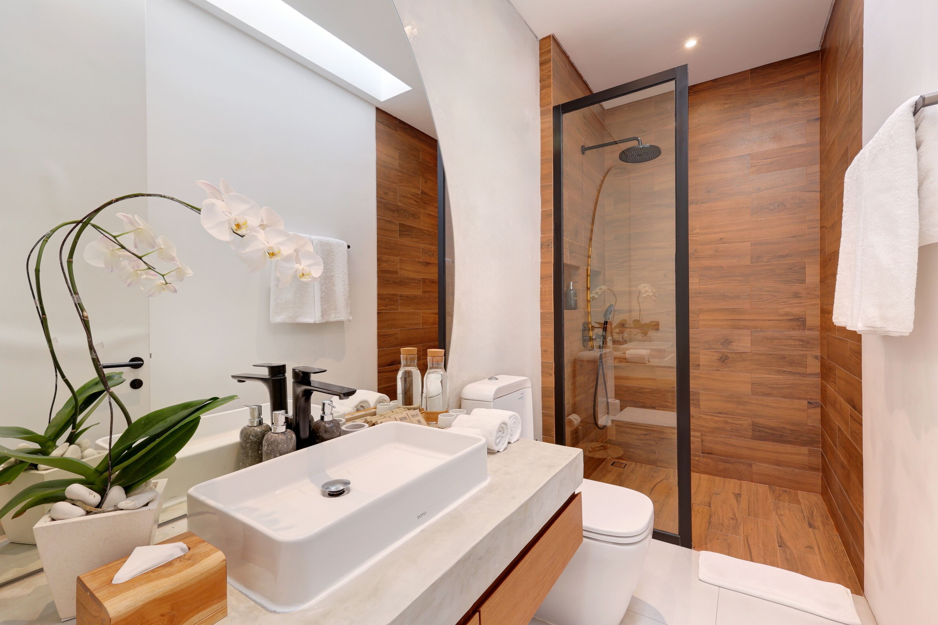 A modern bathroom with a large white sink, a glass-enclosed shower, and wooden paneling.