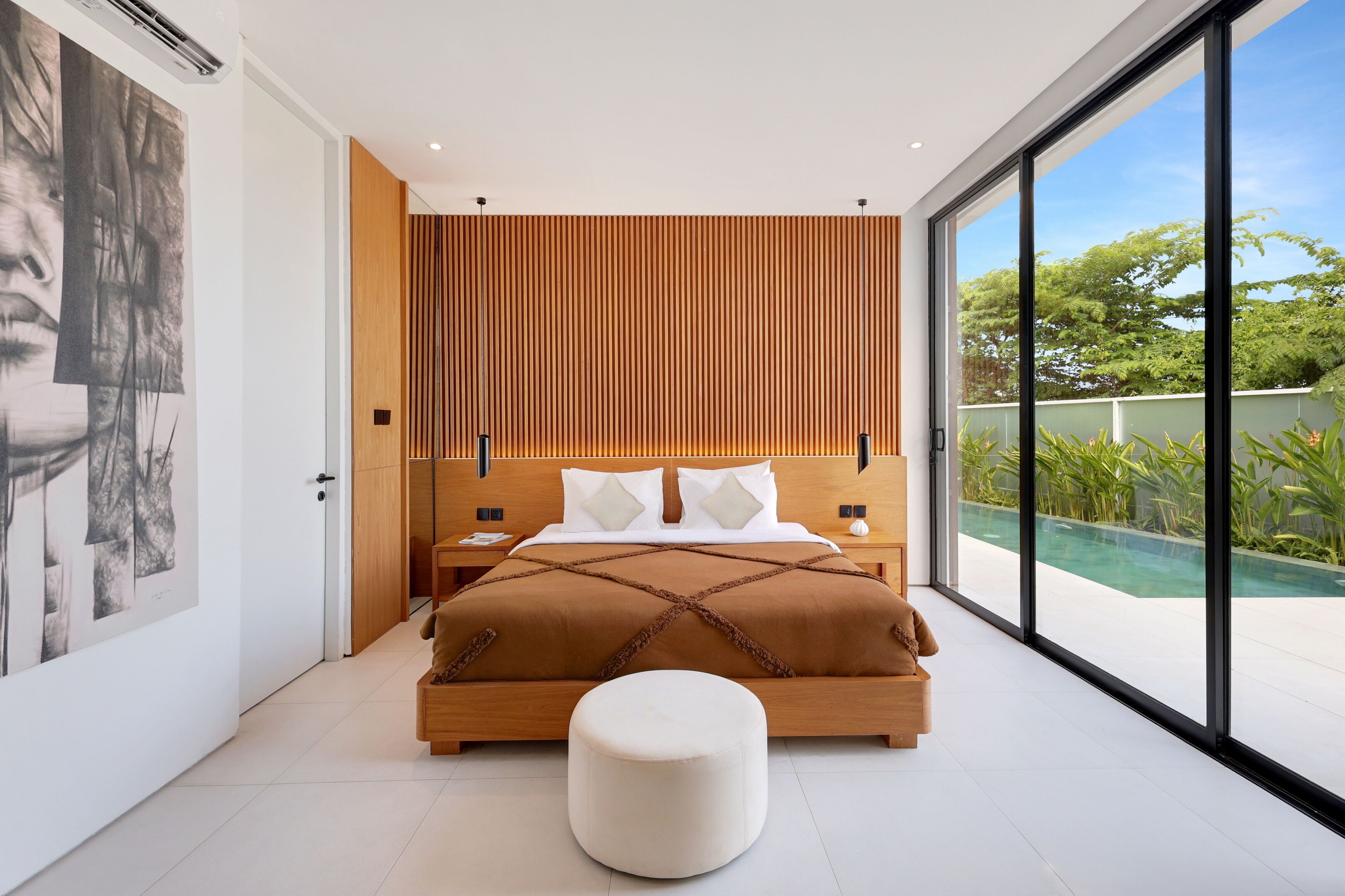 Un dormitorio moderno con una cama grande, pared de paneles de madera y vista a una piscina.