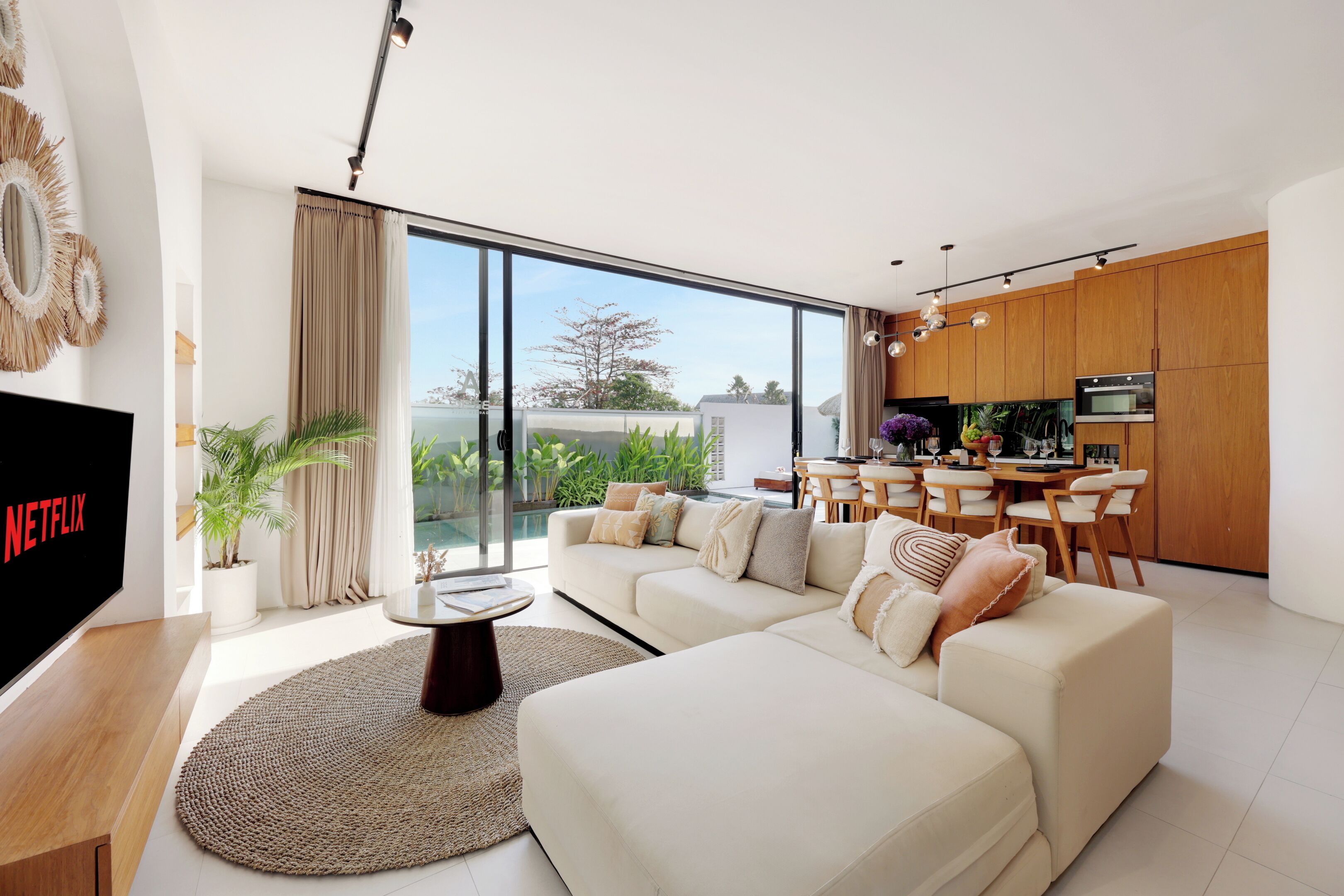 A modern living room with a large sofa, a flat-screen TV, and a dining area with wooden furniture.