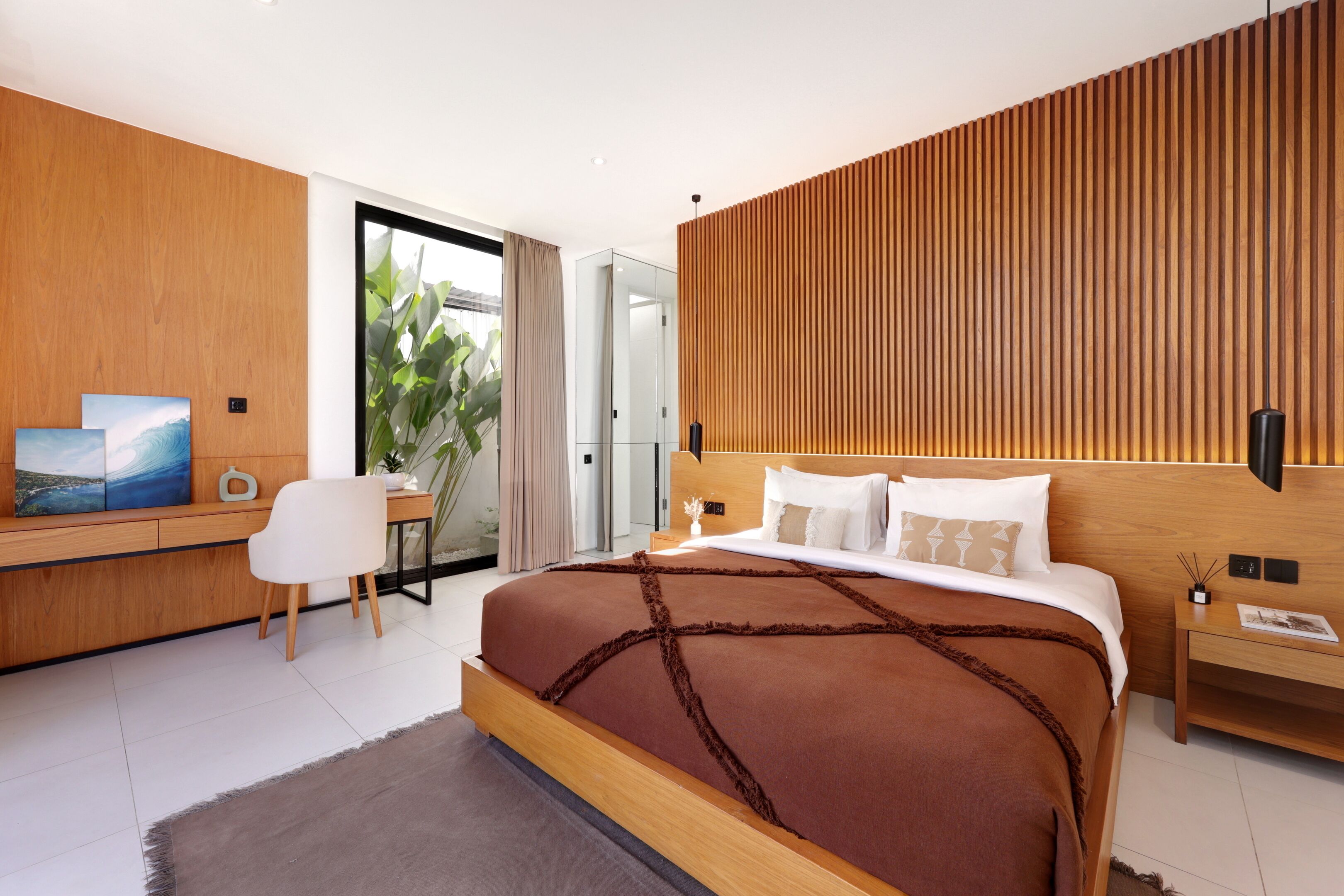 A modern hotel room with a large bed, a desk, and a view of greenery through a sliding door.