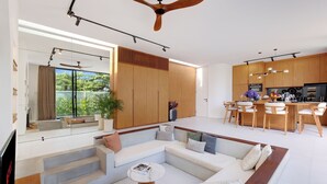 A modern living room with a sofa, coffee table, and a dining area with chairs and a kitchen in the background.