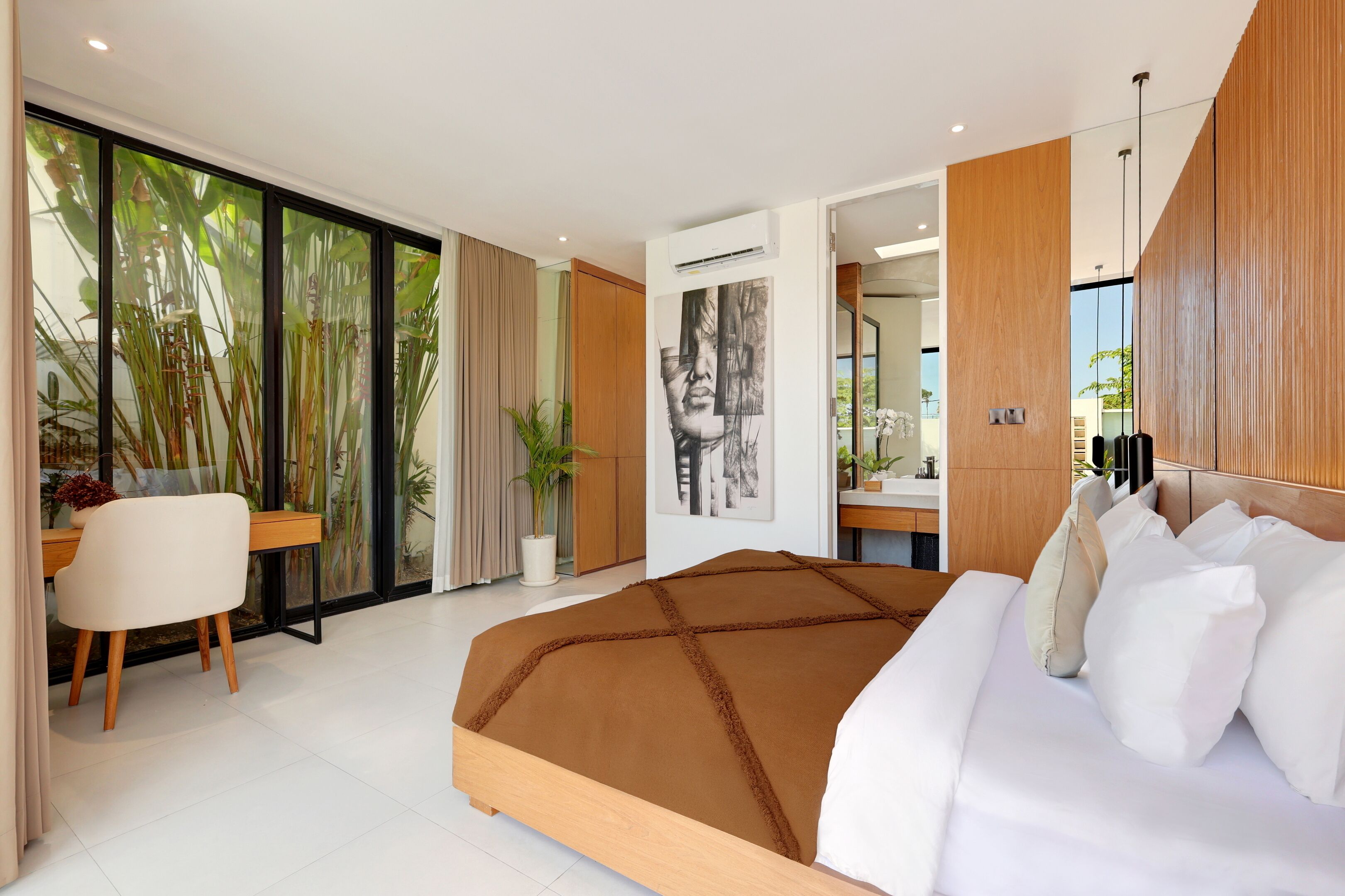 A modern bedroom with a large bed, a desk, and a view of greenery through the window.