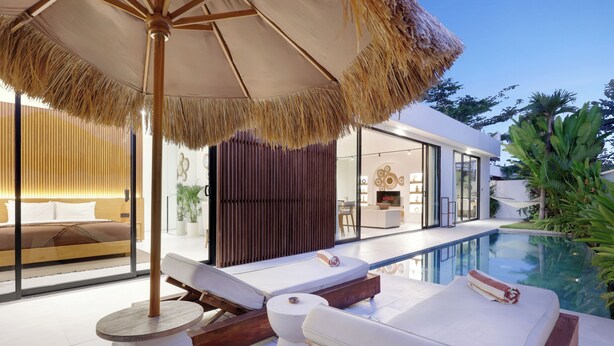 A modern outdoor pool area with lounge chairs and a thatched umbrella.