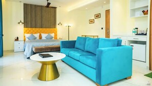 A modern bedroom with a bed, a blue sofa, a gold coffee table, and a kitchenette. - Hotel Southgate Goa (Calangute)